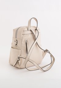 Sac à dos en cuir beige avec quincaillerie argentée, double zip et bretelles ajustables. Il dispose de poches latérales avec une texture lisse et un design minimaliste.