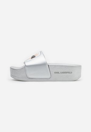Sandalia tipo slide plateada con suela gruesa y banda ancha con diseño esculpido de cara, con la marca "Karl Lagerfeld" en el lateral.