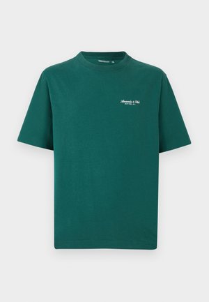 Grønn bomull t-skjorte med korte ermer og rund hals, med hvit brodert logo på brystet og rett hem. Klassisk, uformell design.