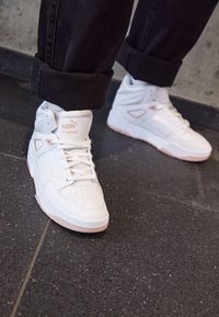 Białe wysokie trampki z wyściełanym kołnierzem, teksturowanymi bokami, perforowanym czubkiem oraz jasnoróżowymi akcentami na podeszwie. Przejrzyste logo na języku.