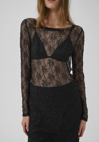 Vestido negro de encaje con mangas largas, una parte superior transparente con un diseño triangular y una sección inferior texturizada con patrones florales.