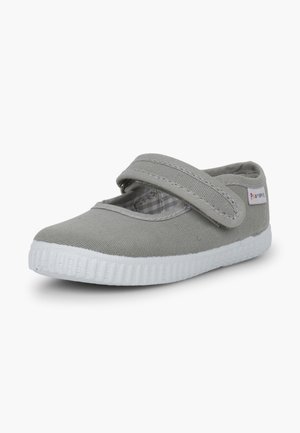 Gray canvas Mary Jane shoe with a Velcro strap, rounded toe, and white rubber sole featuring textured grooves. Checkered lining visible.