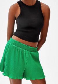 Černý žebrovaný tílko spojené se zelenými skládacími kraťasy s elastickým pasem a vlnitým lemem.