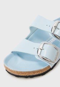 Gros plan d'une sandale bleu clair avec deux boucles argentées réglables, une semelle intermédiaire en liège et une semelle extérieure en caoutchouc noir.