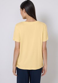 T-shirt en coton jaune avec des manches courtes et un col rond. Texture lisse, coupe décontractée et ourlet légèrement incurvé à l'arrière.