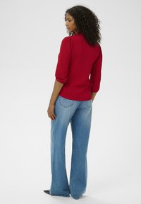 Rød ribbet bluse med pufærmer, båret med lys blå vide jeans. Glat tekstur, tætsiddende silhuet og subtil detalje ved halsudskæringen.