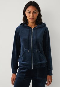 Sudadera con cremallera de felpa en color azul marino, con capucha ajustable, bolsillos frontales y puños de canalé, que presenta una textura suave y lisa.