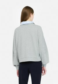 Sweatshirt gris avec une coupe décontractée, des épaules tombantes et un ourlet court. Tissu léger, avec une chemise à col superposée en dessous.