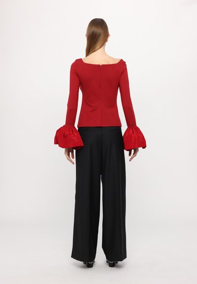 Red fitted top with off-shoulder neckline, flared satin sleeves, and a back fastening. Paired with black wide-leg trousers.