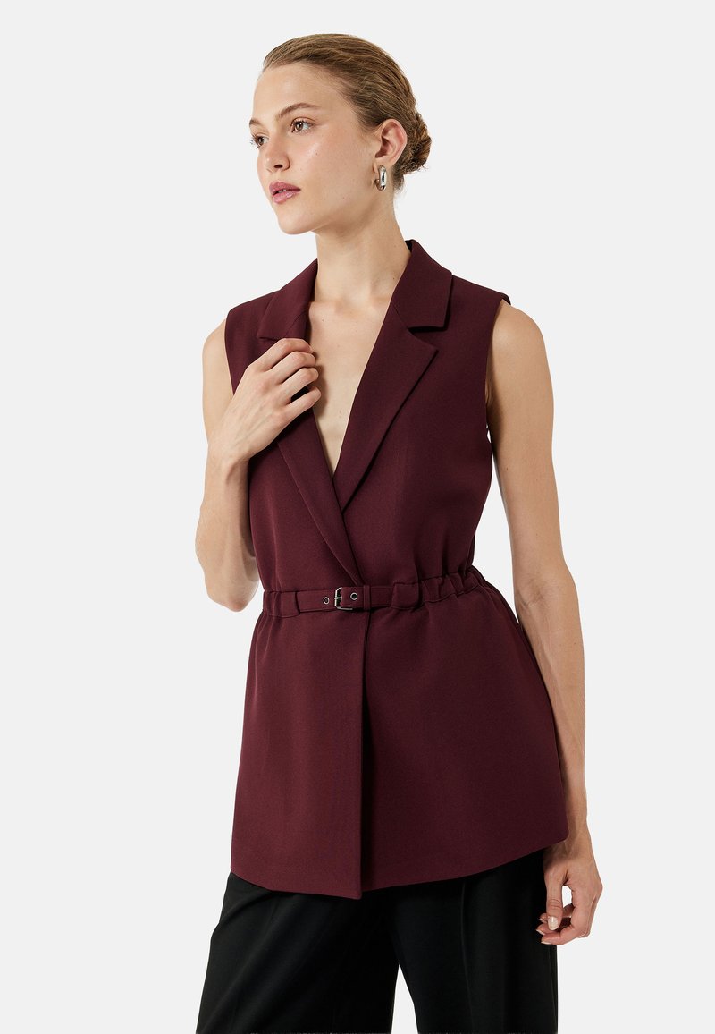 Bordeaux mouwloze blazer met een getailleerde pasvorm, notch revers, tailleband en een split-zoom ontwerp. Gladde wolachtige textuur.