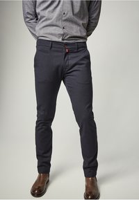 Marina smal passform klädbyxor tillverkade av slät tyg, med framfickor, en liten röd detalj på bälteöglan, i kombination med bruna läderstövlar.