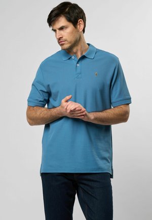 Blauwe polo van een textuurstof met een kraag, voorzien van een klein logo op de linkerkant van de borst, gecombineerd met donkere jeans.