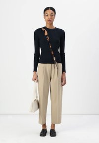 Camiseta negra de manga larga con canalé, con corte lateral y detalle de cordones, combinada con pantalones beige de pierna ancha y mocasines negros, llevando un bolso crema.