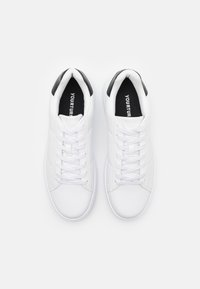 Hvide sneakers med en glat syntetisk overdel, flade snørebånd og en kontrasterende sort hælaccent. Indvendigt er der en sort indersål med logo.
