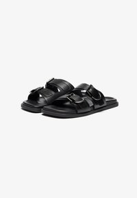 Sandalias de cuero negro con un diseño destalonado, que cuentan con dos correas ajustables y hebillas de plata. Suela plana con una textura suave.