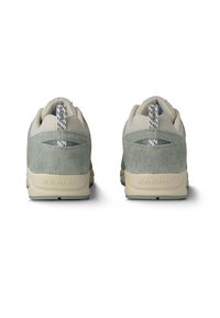 Zapatillas de ante gris y malla beige con cuello acolchado, detalles texturizados y un logo de marca visible en el talón.
