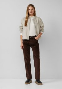 Giacca bomber grigia chiara con zip, abbinata a pantaloni in velluto a coste marroni e stivali neri con plateau. Sotto, una maglietta bianca semplice.