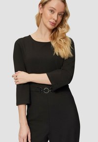 Zwarte jumpsuit met driekwart mouwen, voorzien van een ronde halslijn en een decoratieve riem met ronde hardwaredetails. Soepele textuur.