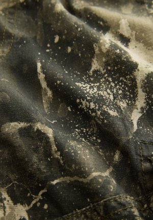 Roheline kangas, millel on tekstuuriga pind ja laiali pritsitud beež mustriga. Suurendus näitab peeneid üksikasju ja täpset õmblust.