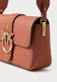 Borsa in pelle marrone texturizzata con un emblema a forma di uccello in tono oro e una chiusura circolare. Presenta una forma strutturata e bordi a contrasto.