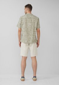 Korte mouwen, lichtgroen patroon shirt met een kraag, gecombineerd met crèmekleurige shorts en casual schoenen. Gegewichtdetails van de stof zijn zichtbaar.