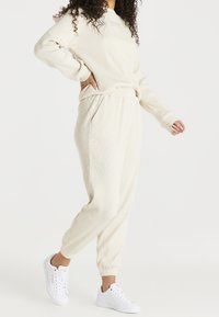 Sudadera y pantalones de chándal de color crema con canalé, que presentan un corte relajado, tobillos acampanados y se combinan con zapatillas blancas.