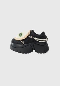 Sneaker platform nera spessa con volto di tessuto attaccato caratterizzato da trucco verde sugli occhi e decorazioni in catena di perle.