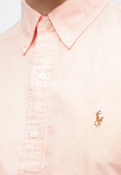 Ανοιχτό ροζ πουκάμισο με κουμπιά από βαμβάκι, με μικρό κεντημένο λογότυπο με αναβάτη αλόγου, λευκά κουμπιά και γιακά με κουμπιά.