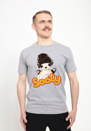 Šedé bavlněné tričko s vyšívaným designem loutkového medvěda s černým kloboukem a červeným logem "Sooty" v tučných písmenech.
