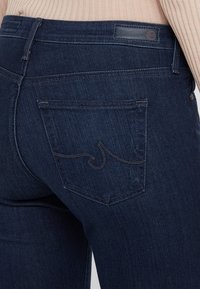 Mörkblå denimjeans med en slät textur, med en böjd broderidesign på bakfickan och en läderlogotyp på midjan.