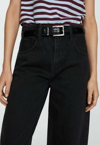 Henkilö, jolla on yllään mustat korkeavyötäröiset farkut, musta nahkavyö ja burgundinpunainen sekä vaaleansinistraiputettu paita, joka on työnnetty vyötärölle.