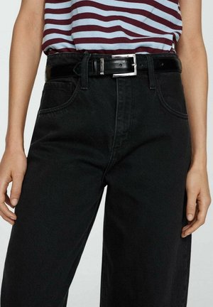 Persona con jeans neri a vita alta, cintura in pelle nera e una maglietta a righe bordeaux e azzurro chiaro infilata dentro.