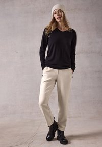 Zwarte langemouwen V-hals top, beige taps toelopende broek met zijzakken en zwarte enkelboots met dikke zolen. Gelaagd crèmekleurig gebreid beanie.