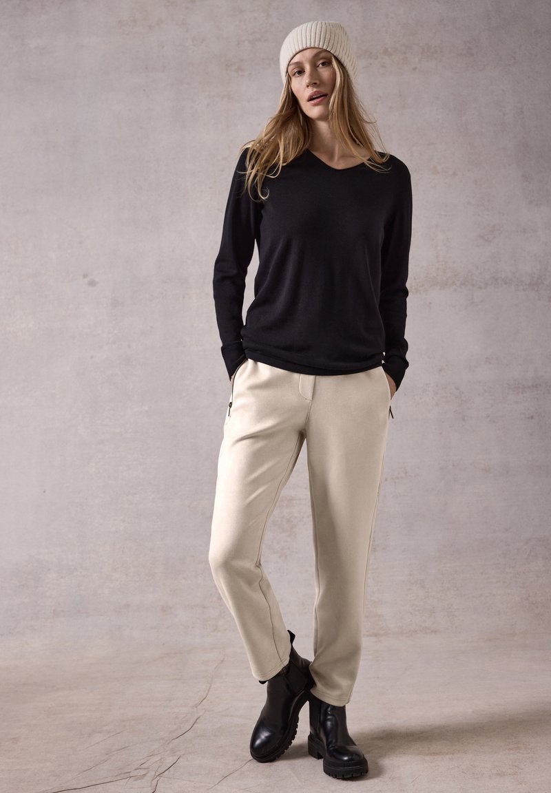 Zwarte langemouwen V-hals top, beige taps toelopende broek met zijzakken en zwarte enkelboots met dikke zolen. Gelaagd crèmekleurig gebreid beanie.