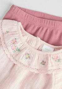 Pametan baby outfit od pamuka koji uključuje svijetlu ružičastu bluzicu s cvjetnim vezenjem i čipkastim rubom, u paru s rebrastim ružičastim hlačama. Vidljiva oznaka branda.