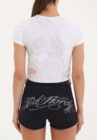 Camiseta blanca ajustada con un sutil estampado de calavera en la espalda; combinada con pantalones cortos de mezclilla negros que presentan un elaborado texto gris en los bolsillos traseros.