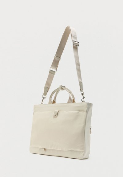 Μπεζ ορθογώνια τσάντα ώμου με ρυθμιζόμενο ιμάντα, επάνω λαβές, μπροστινή τσέπη με κλείσιμο με κουμπί και φερμουάρ στο πλάι.
