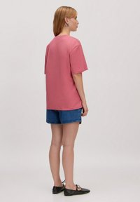 Korte roze katoenen T-shirt met een ronde hals, korte mouwen en een ontspannen pasvorm, gecombineerd met denim shorts en zwarte platte schoenen.