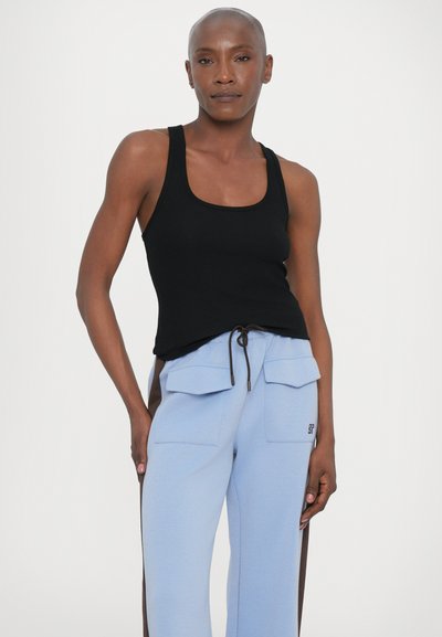 Top sin mangas negro de canalé combinado con pantalones de un azul claro que tienen dos grandes bolsillos frontales y un cordón ajustable en la cintura.