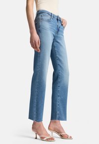 Ljusblå jeans i rak modell, med blekt utseende, rå fåll och framfickor; matchade med vita sandaler med remmar.