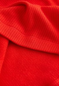 Czerwona tkanina o teksturowanej powierzchni, z gładką i żłobioną sekcją, pokazująca szwy oraz jednolitość koloru.