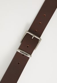 Brauner Ledergürtel mit einer silbernen Metallschnalle. Verfügt über mehrere Löcher zur Größenanpassung und einem "Levi's"-Logo auf der Schnalle.