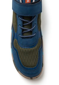 Zapatilla azul y verde oliva con tela de punto, cordones oscuros azules con patrón, y una suela beige con detalles de camuflaje en azul y marrón.