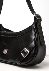 Borsa in pelle nera con dettagli in fibbia argento e tracolla regolabile, cerniera parzialmente aperta su uno sfondo bianco.