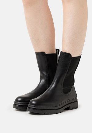 Bottes noires en cuir jusqu'à la cheville avec des panneaux latéraux élastiques et une semelle en caoutchouc texturée. Fini lisse avec des détails de couture subtils.