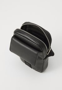 Schwarze Lederhandtasche mit strukturierter Oberfläche, Reißverschluss, flacher Vorderseite-Tasche und verstellbarem Trageriemen. Kompakte Bauweise mit minimalen Hardware-Details.