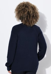 Pull en maille bleu marine à manches longues et texture côtelée, avec un col rond et un ourlet allongé à l'arrière.