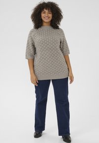 Lichtgrijze gebreide trui met een textuurpatroon van diamanten, geribbelde boorden en zoom; gecombineerd met donkerblauwe uitlopende jeans en zwarte schoenen.