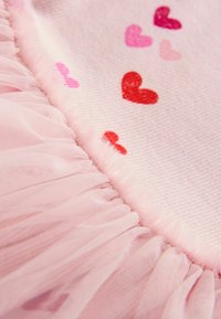 Rózsaszín, puha tapintású szövet, amelyen piros és rózsaszín szívek vannak elszórva. Az egyik szélén fodros tüllszegély ad mélységet.