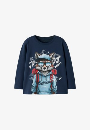 Marineblauwe longsleeve t-shirt met een fox-graphic die een zonnebril draagt en een blauwe hoodie met rode rugzakaccenten, samen met een buitenactiviteiten-thema tekst.